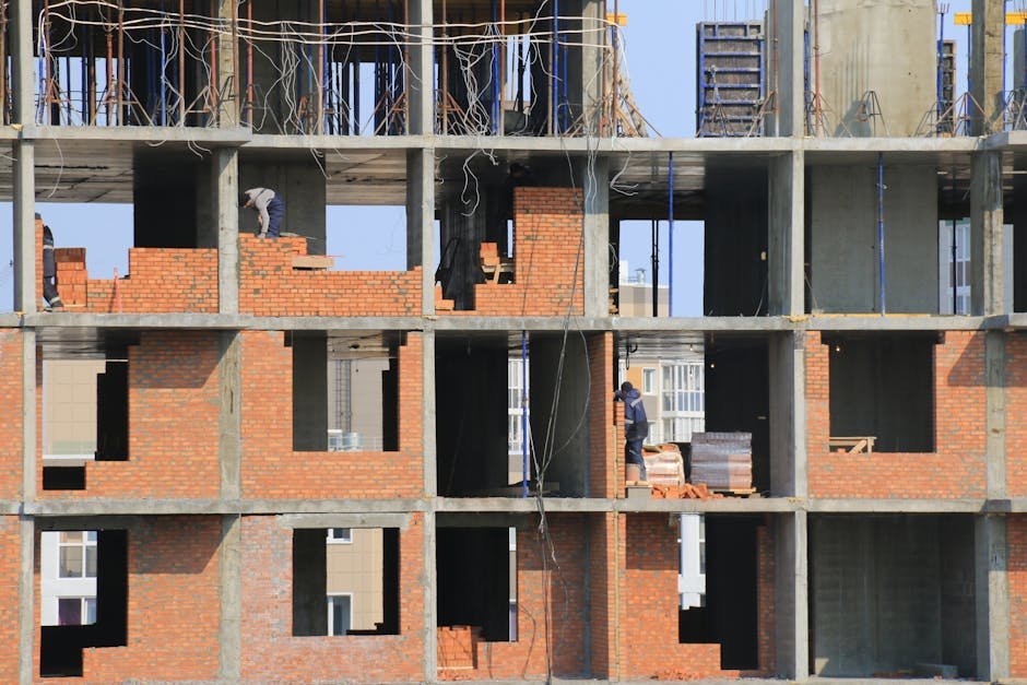 Workers engaged in bricklaying on a multi-story building under construction in an urban area.